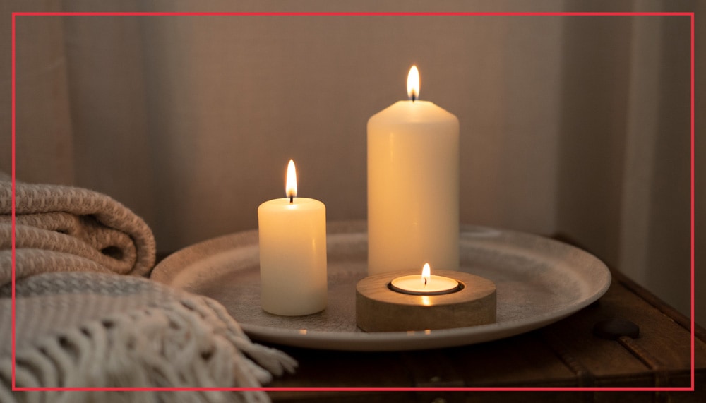 Angezündete weiße Kerzen auf Teller mit Teelicht und dekorativer Decke