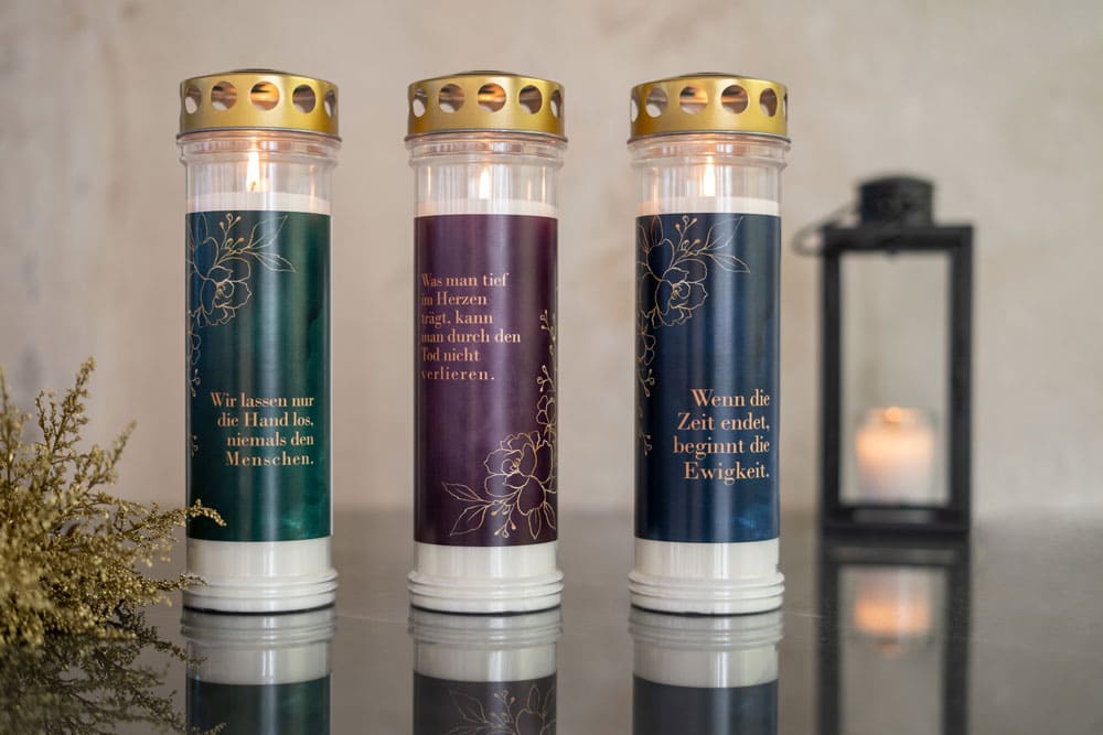 Angezündete Kerze mit gold-schimmernden Motiven auf Marmor und Kerze in Laterne