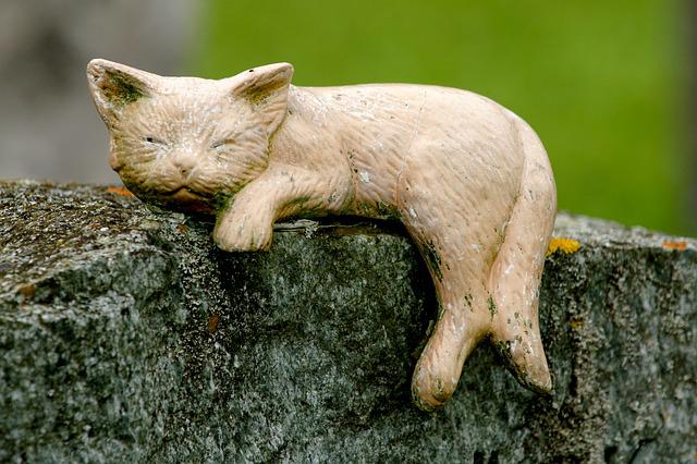 schlafende Katzenfigur auf einer Steinmauer