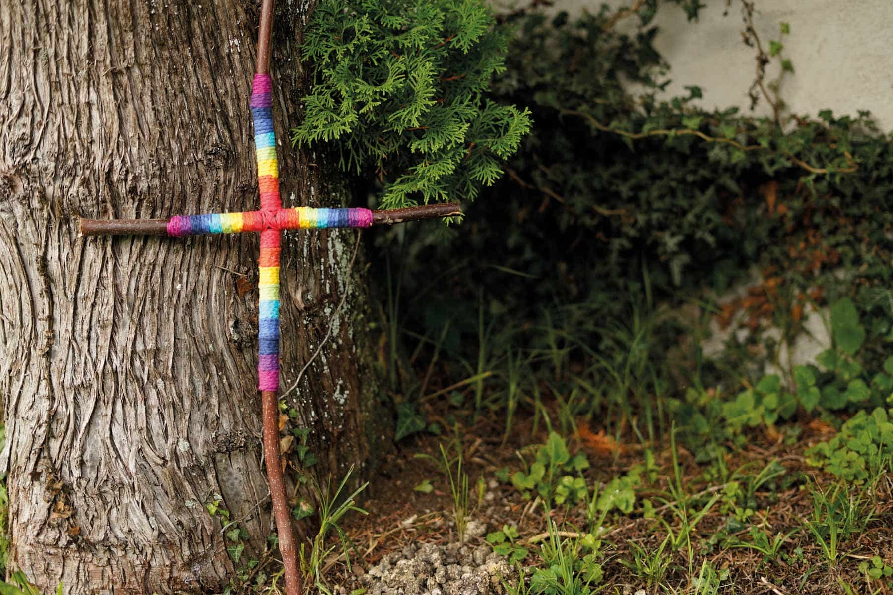 Buntes Holzkreuz lehnt an einem Baumstamm