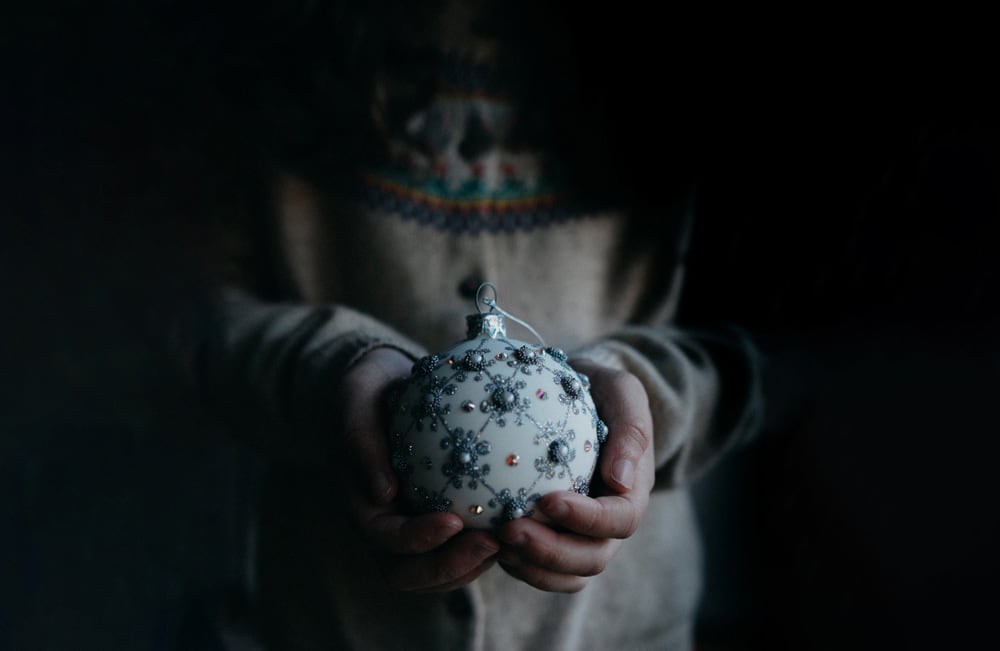 Kind hält Christbaumkugel vor schwarz